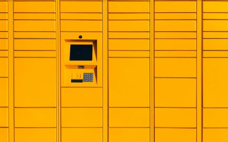 <span class="uk-h4">Bright yellow smart parcel delivery lockers featuring a central electronic touchscreen interface and metallic keypad</span>