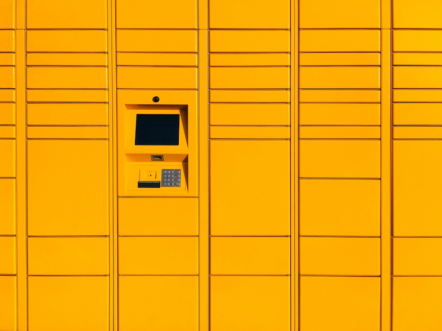 Bright yellow smart parcel delivery lockers featuring a central electronic touchscreen interface and metallic keypad