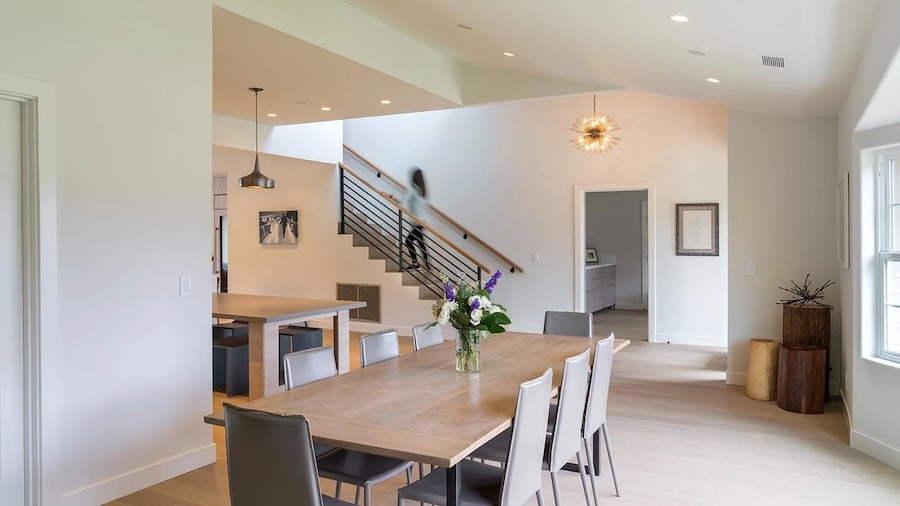 Open-concept dining area with a table, a chandelier, pendant lights, and a staircase leading to the upper level.