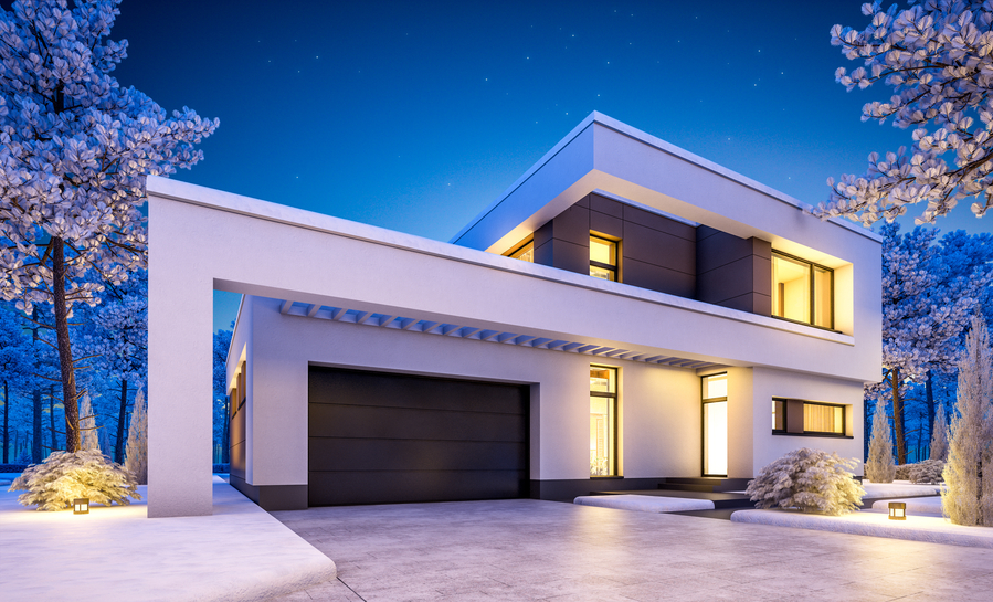 A modern two-story home lit at night with warm interior light, path lighting, and snow-dusted trees
