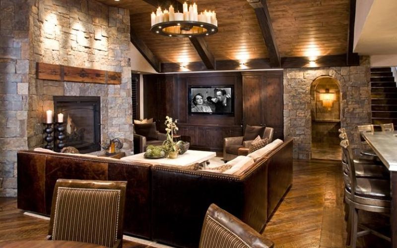 <span class="uk-h4">Rustic luxury media room with a leather sectional, stone fireplace, wall-mounted TV, and warm layered lighting.</span>